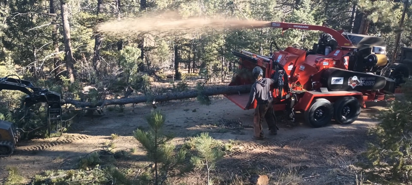Industrial wood chipper blowing chips into the forest during slash removal
